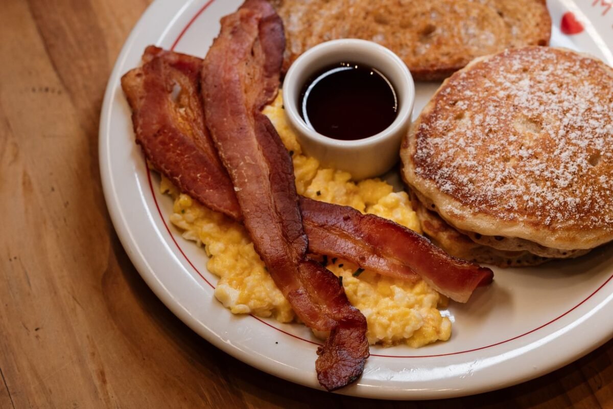 Scrumptious breakfast of pancakes, bacon, and scrambled eggs on a rustic table.