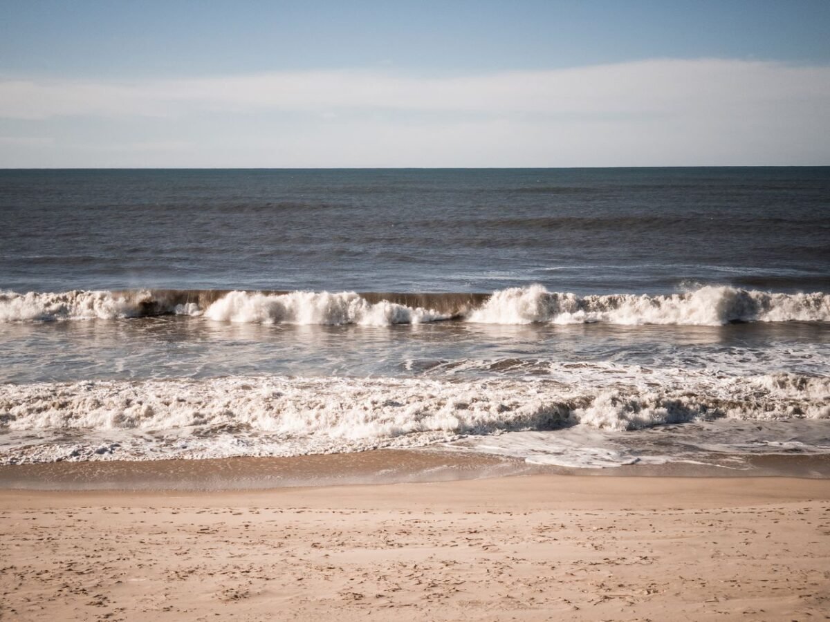 A tranquil scenic view of waves crashing on an empty sandy beach under a clear blue sky.